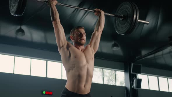 Young male athlete lifts a barbell above his head, weight training