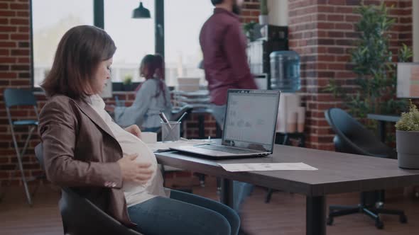 Pregnant Business Woman Working on Laptop Using Documents for Marketing Strategy