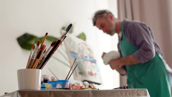 Closeup of Brushes Standing in Jar on Table at Background Man Draws Picture on Canvas