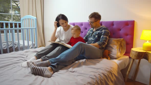 Mother, Father and Boy at Home Spending Time Together Reading Book in Bed