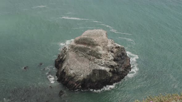 High angle slow motion wide shot of waves crashing into a huge rock in the Pacific.