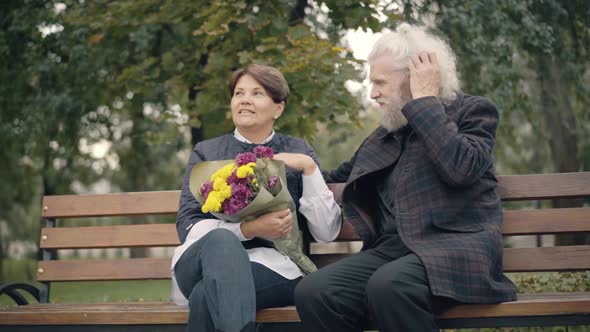 Positive Relaxed Couple of Caucasian Retirees Sitting on Bench in Autumn Park Talking