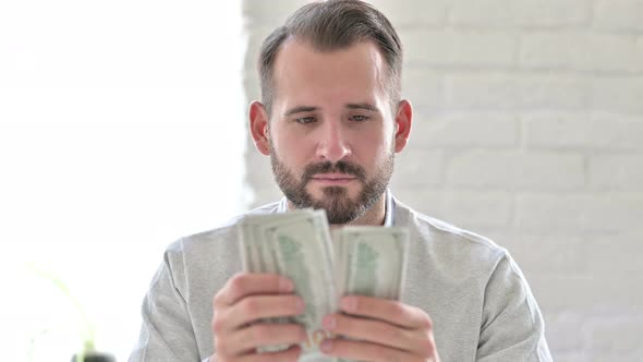 Portrait of Focused Young Man Counting Dollars