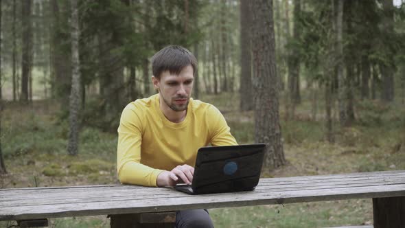 Man Looking at Laptop Screen in Forest