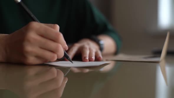 Closeup Hands of Unrecognizable Young Woman Writing Handwritten Wishes on Christmas Card Sitting at