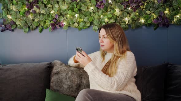 Woman Sits on the Couch and Looks at Something on the Phone