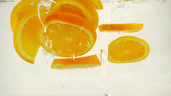 Juicy Orange Slices Fall Into Water with Splashes and Bubbles, Slow Motion Close-up