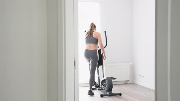 Rear view of young woman on cross trainer at home