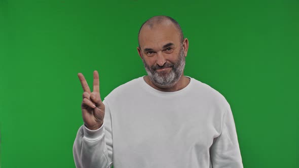 Cheerful Senior Man Showes Victory Sign on Isolated Green Background