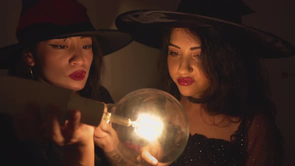 Two Colombian Women In Halloween Costume Wearing Witch Hat Moving Their Hands Around The Transparent