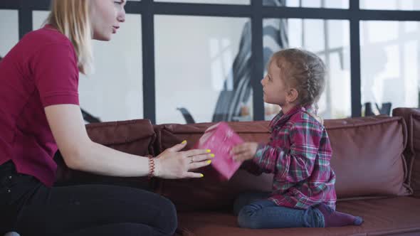 Side View of Joyful Woman and Little Girl Shaking Pink Gift Box. Portrait of Blond Caucasian Mother