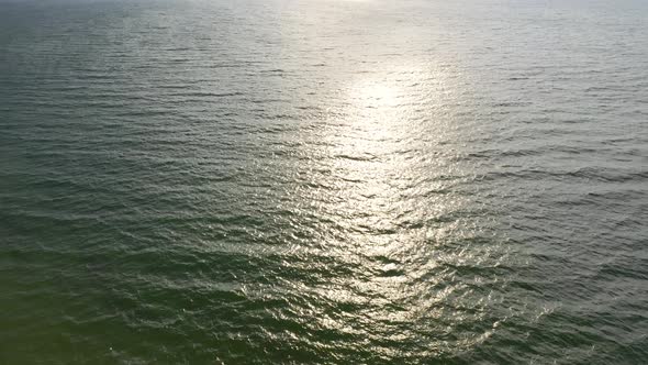 AERIAL: Locked Shot of Waves Crashing on the Surface of Reflective Sea 