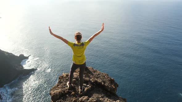 Young Woman Raising Her Arms on Beautiful Steep Cliff Over the Ocean. Lady on the Summit