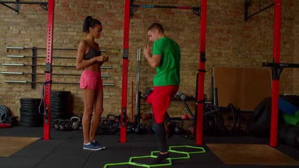 Fitness Trainer Showing Cardio Workout to Black Fit Female Using Agility Ladder