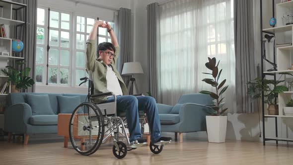 Asian Man Sitting In A Wheelchair And Stretching At Home