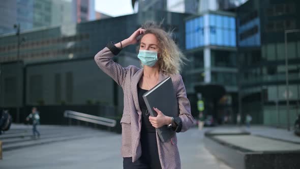 Young woman walks through the city wearing a medical mask and holding a folder