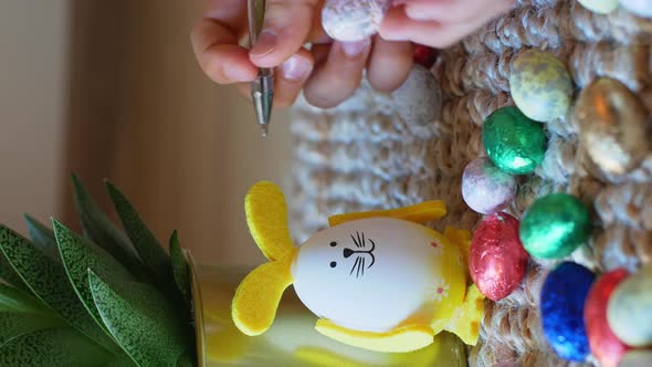 Girl draws a pattern on an Easter egg next to an egg in the shape of a rabbit