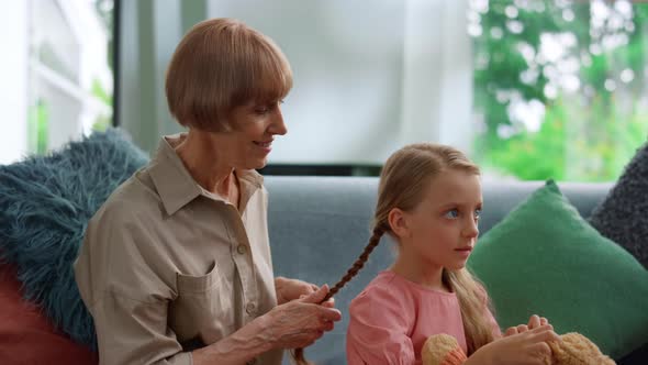 Happy Grandmother Braiding Pigtail for Granddaughter at Home. Smiling Family