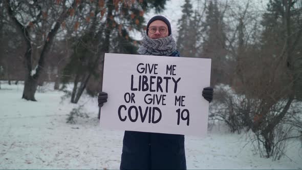 A man in the Park is Holding a Sign Give me Liberty or Give Me Covid 19. Protest