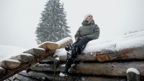 Calm Woman Enjoying the Snowfall in a Winter Forest in the Mountains Sitting on a Snowcovered Wooden