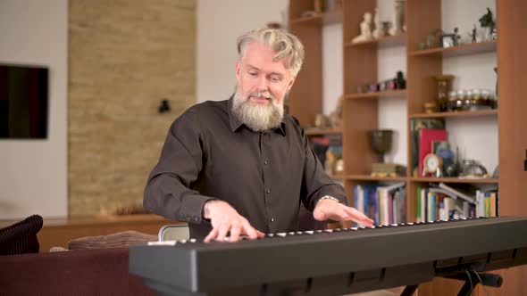 adult solid gray-haired man with a stylish beard plays the electronic piano