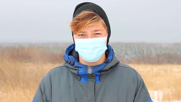a Young Caucasian Teenager Man Dressed in Warm Winter Clothes Stands on the Street in a Blue Medical