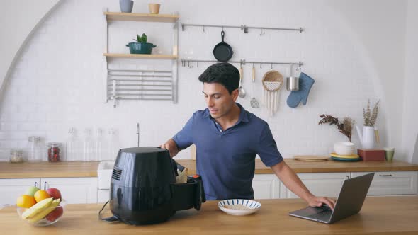 Man Using Air Fryer and Laptop in Kitchen