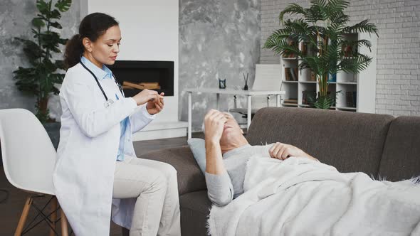 Elderly Man Lying on Couch Measuring Temperature Giving Thermometer to Doctor Female Who Saying That