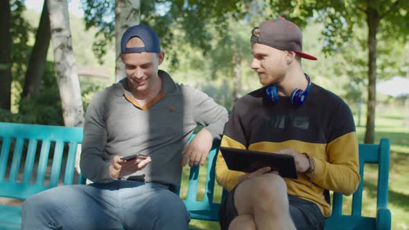 Gay Couple with Gadgets Enjoying Leisure in Park