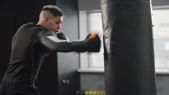 Athletic and Concentrated Young Man Boxer Hitting the Punching Bag in the Gym
