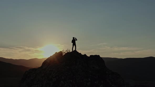 Silhouette of a Man Standing on the Top of a Mountain in the Last Rays of the Sunset in the