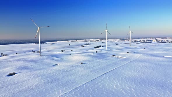 Wind turbines on snowy field in sunny winter day.