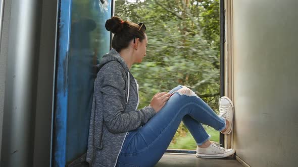 Young Woman Sits Near Open Doors of Moving Train and Looks Out at Beautiful Nature. Female Tourist