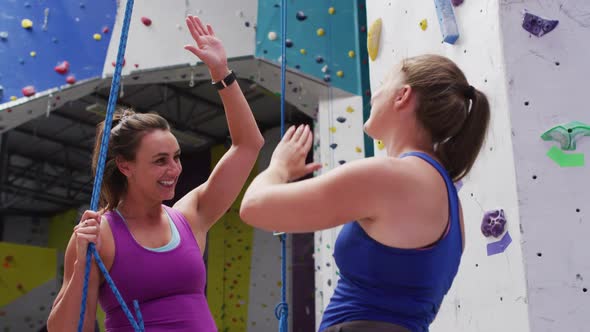 Two caucasian women talking and high fiving at indoor climbing wall