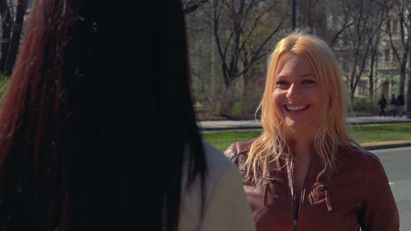 A Young Caucasian Woman and a Young Asian Woman Talk in a Street in an Urban Area