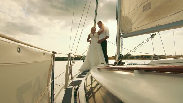 Newlyweds Stand on a Bow of a Sailing Yacht Like in Titani. The Bride Put Her Head on the Groom's