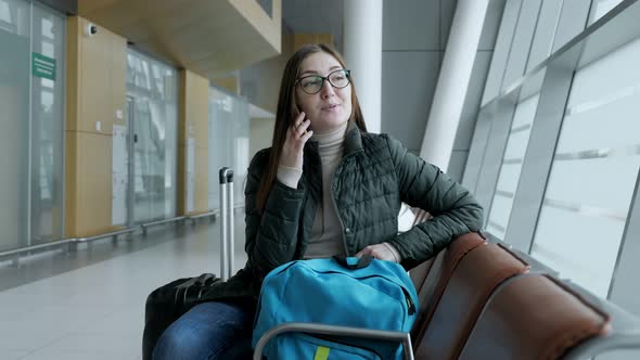 Happy Woman is Talking on Mobile Phone Waiting Her Flight in Airport