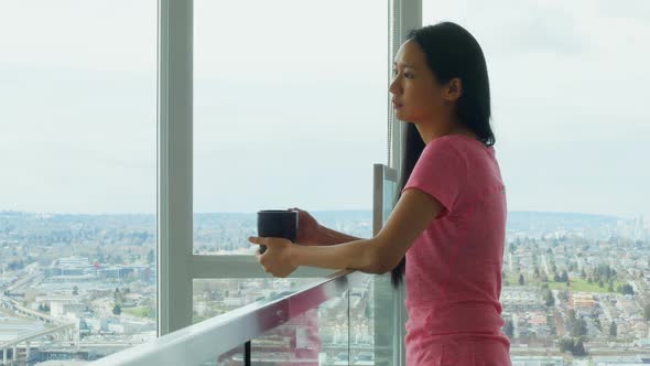 Woman looking through window while having cup of coffee 4k