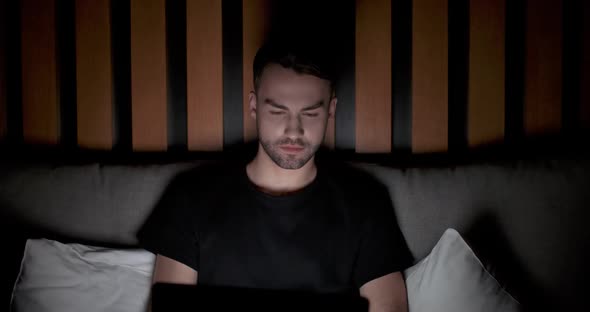 Young Man Lying on the Bed and Working on a Laptop Types Text on the Keyboard Works at Night Remote