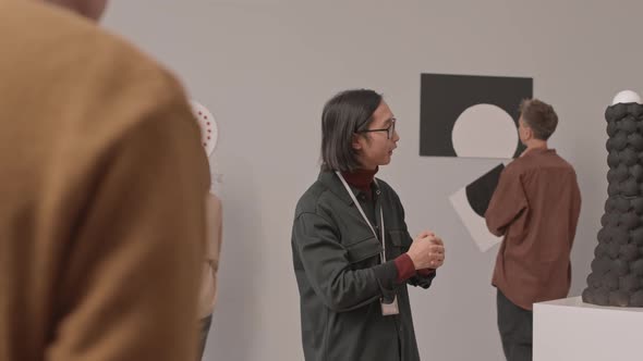 Asian Guide Talking to Tourists in Modern Art Museum