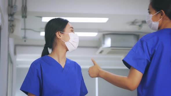 Young Asian Nurse Wearing Scrubs Uniform with Surgical Mask Showing Thumbs Up Gesture in Hospital