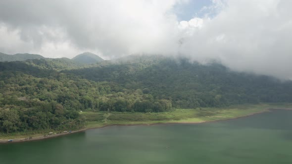 Drone Over Lake Towards Forest Covered Hills Under Cloud