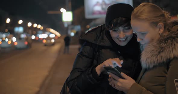 Women Watching Something on Mobile While Waiting at Bus Stop in the Evening