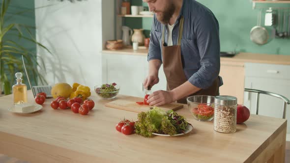Man With Beard Cutting Tomato on Cutting Board in His Kitchen