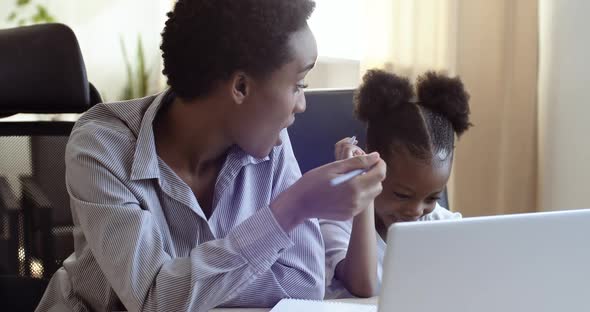 African Black Woman Mom Helping Cute Beloved Daughter Schoolgirl with Homework Sitting Together at