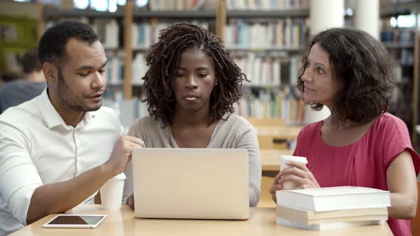 Thoughtful People Talking While Using Laptop at Library