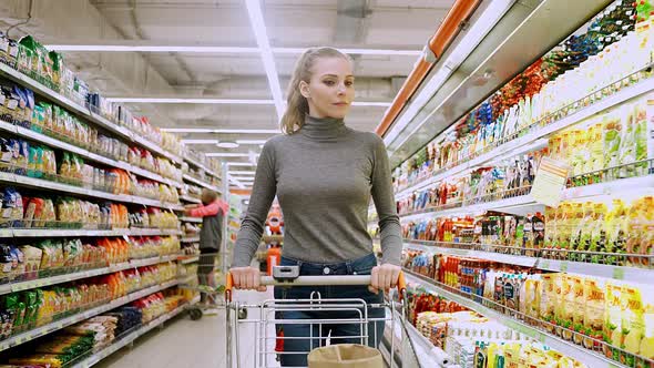 Young Female Walks Between the Shelves in a Grocery Store Visiting a Supermarket a Woman Walks with