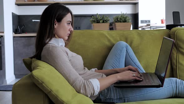 Young Woman in a Beige Sweater Relaxing on the Couch While Holding a Laptop at Home Office