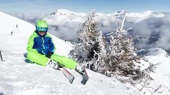 Skier Boy Sit on Top of the Mountain in Clouds Lift Hands Up