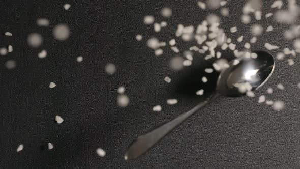 Spoon With Salt Falls On A Black Table